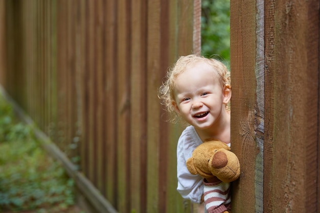 Cheerful girl looks out through a hole in the fence in the ranch. Copy space.