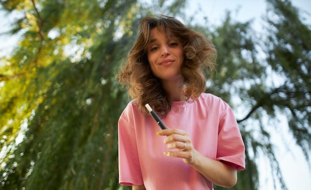 Cheerful girl in a pink t-shirt with an electronic cigarette in the park.