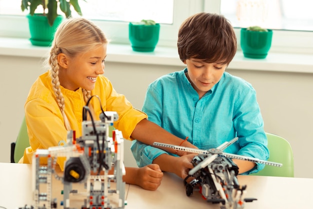 Cheerful girl playing with construction helicopter of her classmate