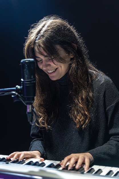 Cheerful girl in the process of recording musical content in the studio, recording voice into a professional microphone, the concept of learning piano online.