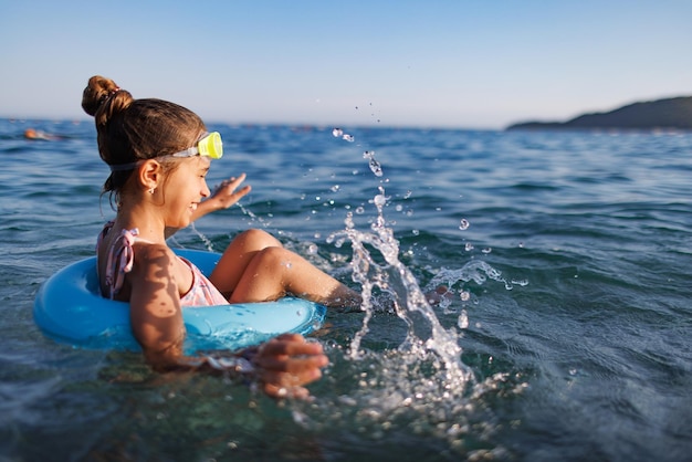 Cheerful girl sits in an inflatable circle and splashes with water in the sea