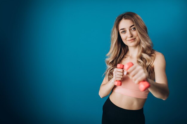 Cheerful girl in sport outfit holding dumbbells in studio