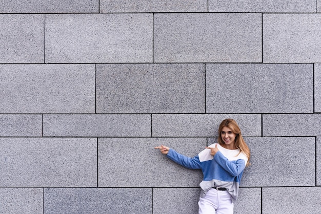 Cheerful girl at the street, show a big sale, or nice offer. Advertise concept. People, travel and tourism - woman on city street and girl show with her finger something over gray wall background