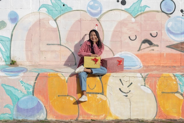 The cheerful girl wearing party hat with gift box sitting on colorful background