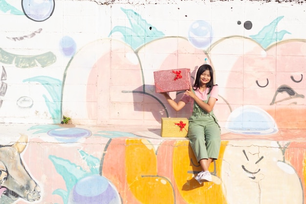 The cheerful girl wearing party hat with gift box sitting on colorful background