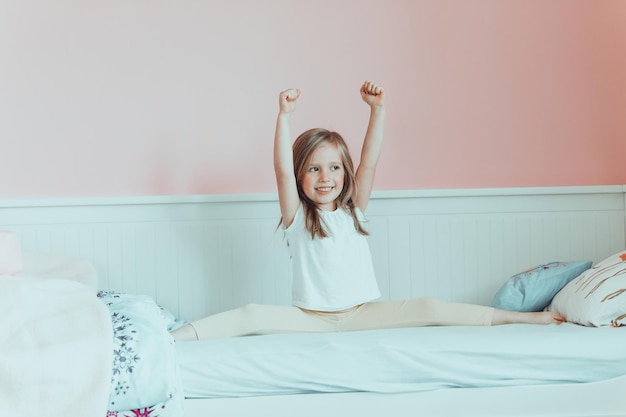 Photo cheerful girl with arms raised sitting on bed at home