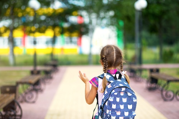 バックパックを背負って、校庭の制服を着た元気な女の子がフレームに戻ります。