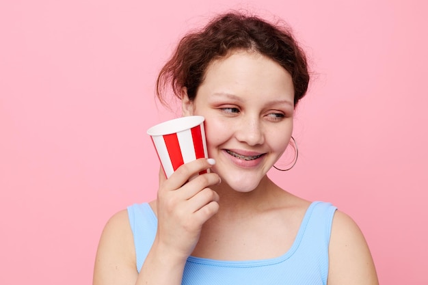 Cheerful girl with a disposable multicolored glass on a pink background