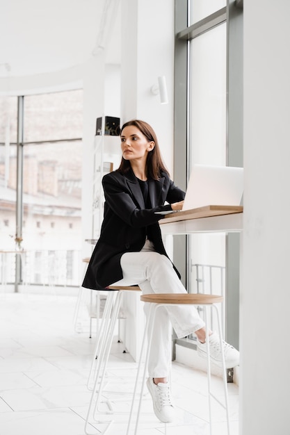 Cheerful girl with laptop have a break at work and dreaming in\
cafe young woman is relaxing and thinking about new ideas in white\
office