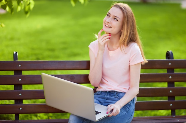 Cheerful Girl with laptop sitting on bench in Park 