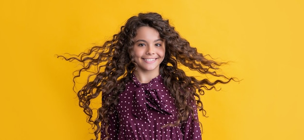 Cheerful girl with long brunette curly hair on yellow background