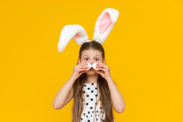 A cheerful girl with rabbit ears on her head with chicken eggs in her hands on a yellow background Funny happy kid