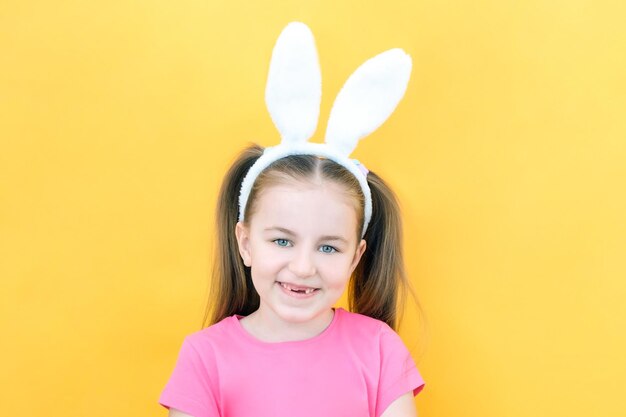 Photo cheerful girl with rabbit ears on her head on a yellow background funny crazy happy child easter child preparation for the easter holiday promotional items copy space for text mockup