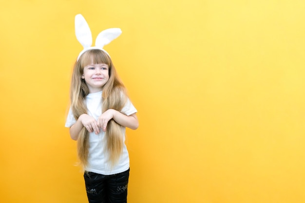 Cheerful girl with rabbit ears on her head on a yellow background Funny crazy happy child Easter child Preparation for the Easter holiday promotional items copy space for text mockup