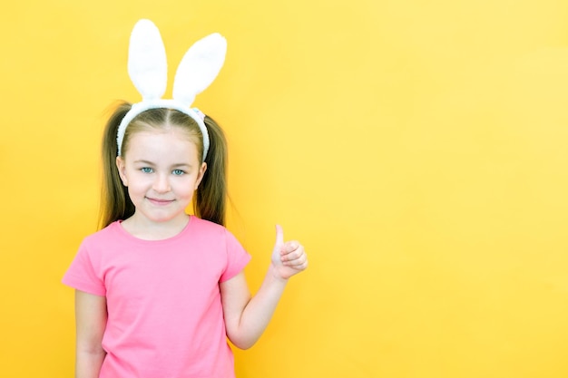 黄色の背景に彼女の頭にウサギの耳を持つ陽気な女の子面白い幸せな子は、テキストのモックアップのための空きスペースのコピースペースのように表示されます