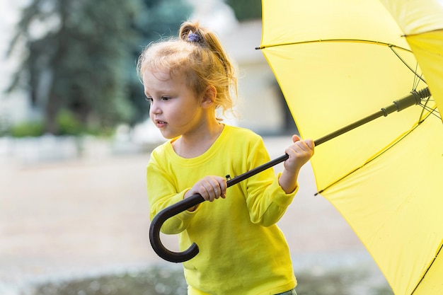 Веселая девушка в желтой одежде с ярким зонтиком гуляет после дождя