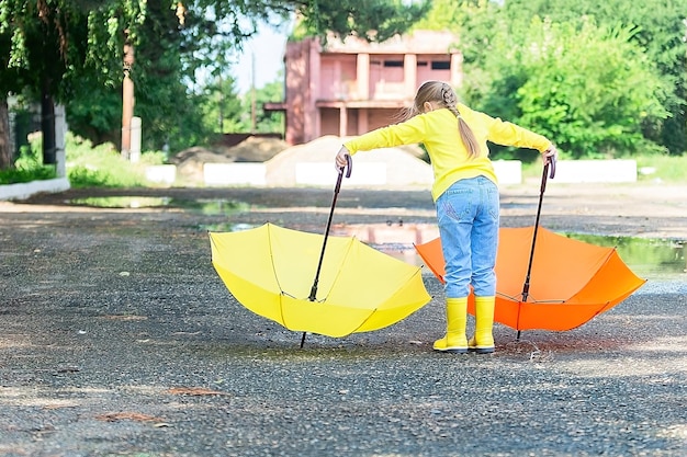 A cheerful girl in yellow clothes and with two bright umbrellas walks around the city