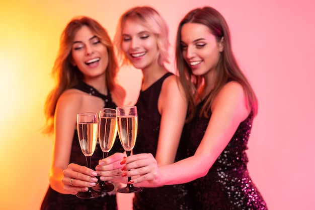 Le ragazze allegre tengono bicchieri di champagne celebrano il natale sul fuoco selettivo di sfondo a colori