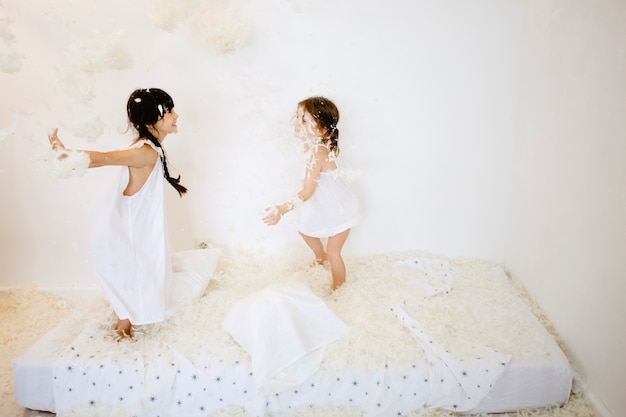 Photo cheerful girls throwing feathers on mattress