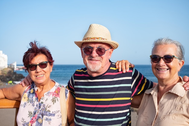 Cheerful group of adult senior people wearing straw hats and sunglasses enjoy sea holiday excursion