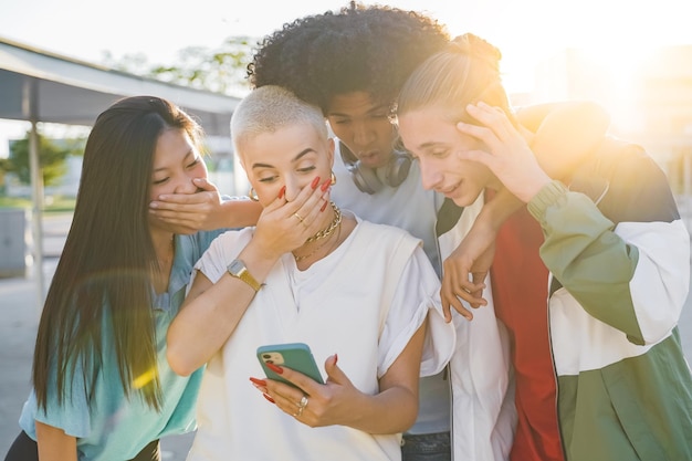 Gruppo allegro di amici alla ricerca di smart phone sorpresi ed eccitati all'aperto sorridente giovani