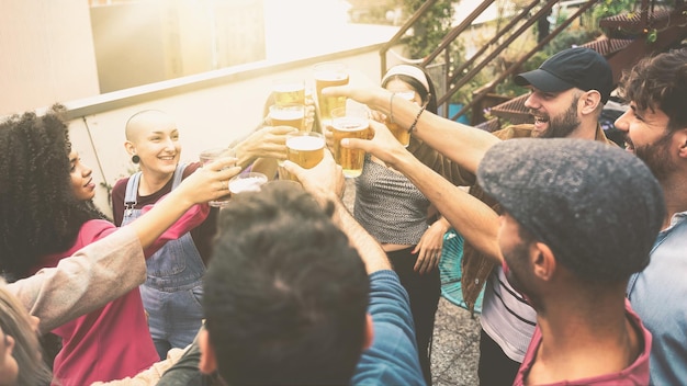 ビールで乾杯する異人種間の学生の陽気なグループ。ユースホステルの屋上でハッピーピープルパーティー。太陽フレアでフィルタリングされた画像