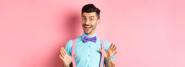 Cheerful guy in bowtie showing his suspenders and smiling happy feeling upbeat standing excited over