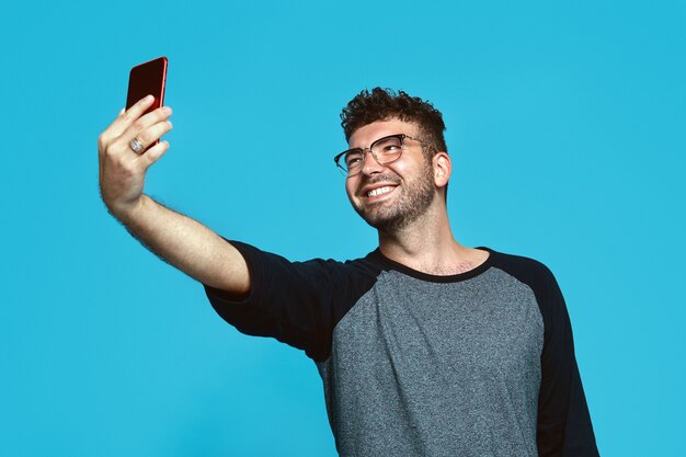 Cheerful guy taking selfie with smile isolated over blue wall