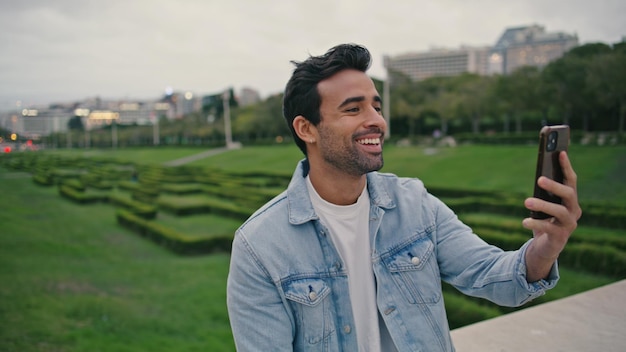 Cheerful guy video calling by smartphone in green park close up smiling man