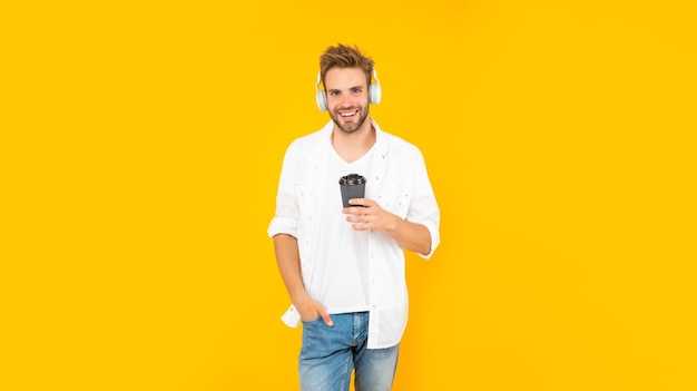 Cheerful guy with bristle listen music drink coffee on yellow background modern device