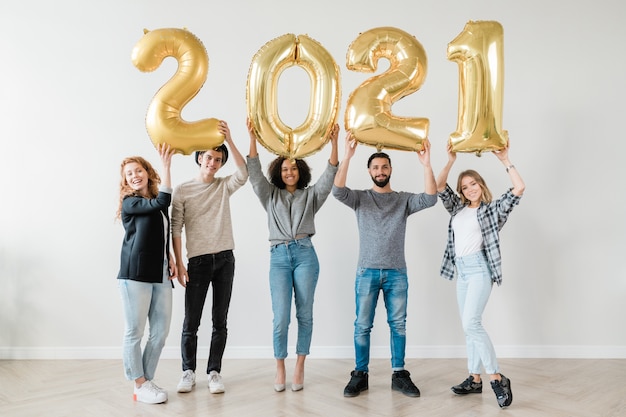 Photo cheerful guys and girls holding number of new year in raised hands