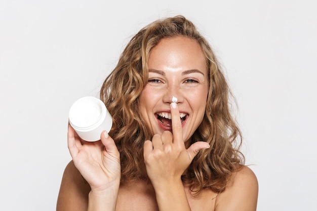 cheerful half-naked woman making fun with facial cream isolated over white wall