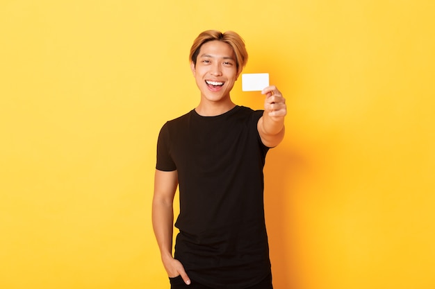 Cheerful handsome asian guy smiling pleased and showing credit card