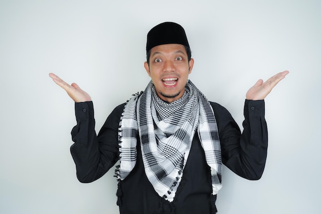 즐거운 잘생긴 아시아 무슬림 남자가 아랍의 <unk>을 입고 손가락을 가리키는 소르반을 쓰고 있습니다.