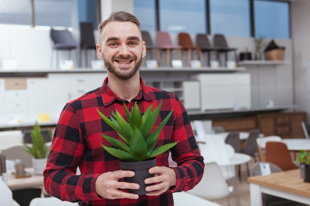 陽気なハンサムなひげを生やした男がカメラに笑顔、鉢植えのアロエを保持