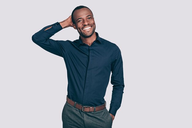 Cheerful and handsome. Handsome young African man holding hand behind head and smiling while standing 