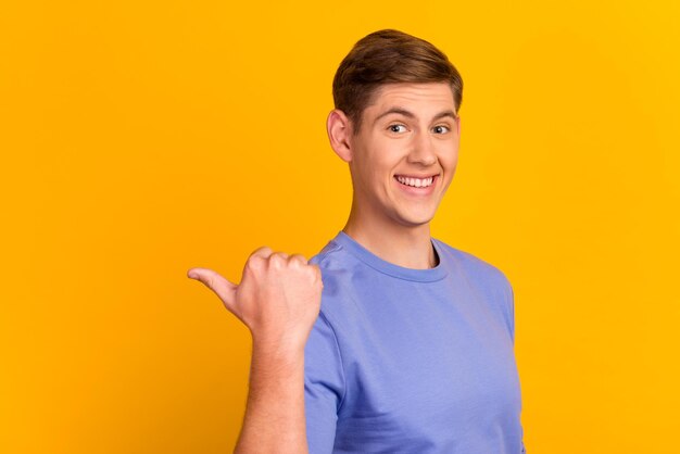 Cheerful handsome man showing direction and pointing with finger thumb on yellow color background