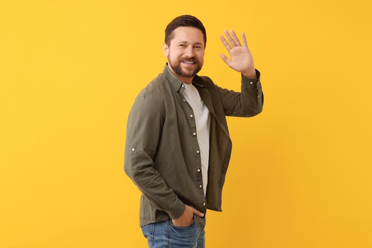 Photo cheerful handsome man waving on orange background