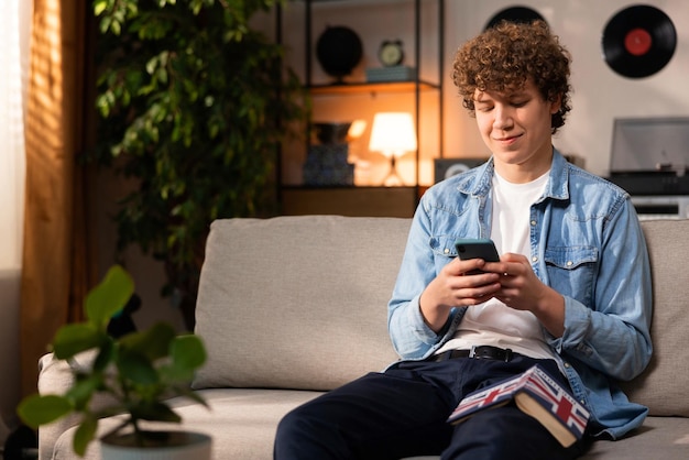 A cheerful handsome teenage boy chats with his friends on his smartphone