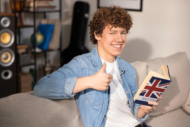 A cheerful handsome teenage boy learns english using a dictionary a student is preparing for exams