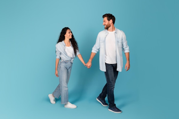 Cheerful handsome young european bearded guy leads the hand of lady in casual isolated on blue background