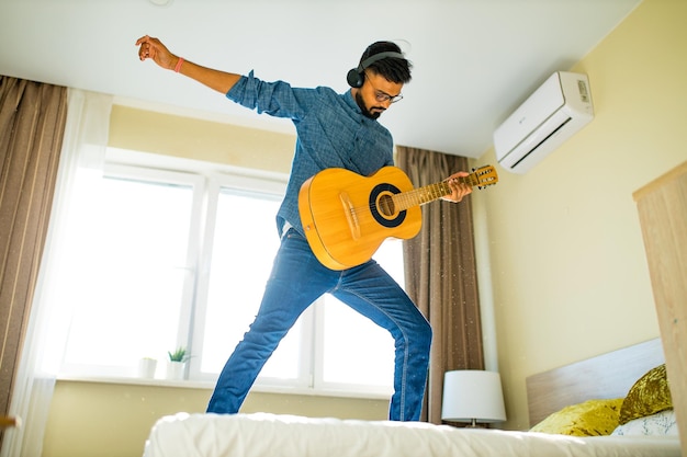 Cheerful handsome young man playing guitar and smiling in new cozy apartment