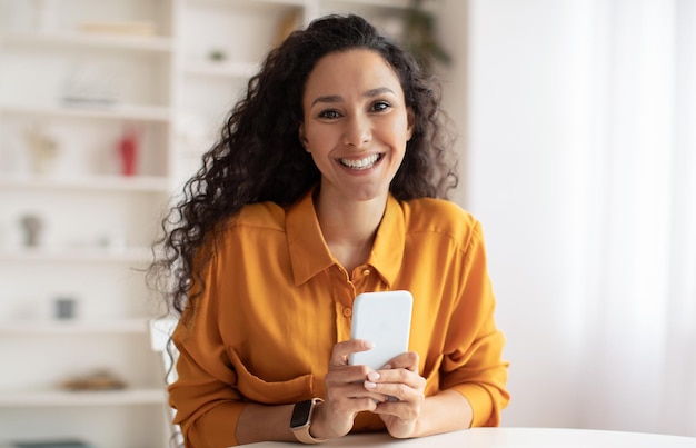 Cheerful happy brunette businesswoman using smartphone in modern office