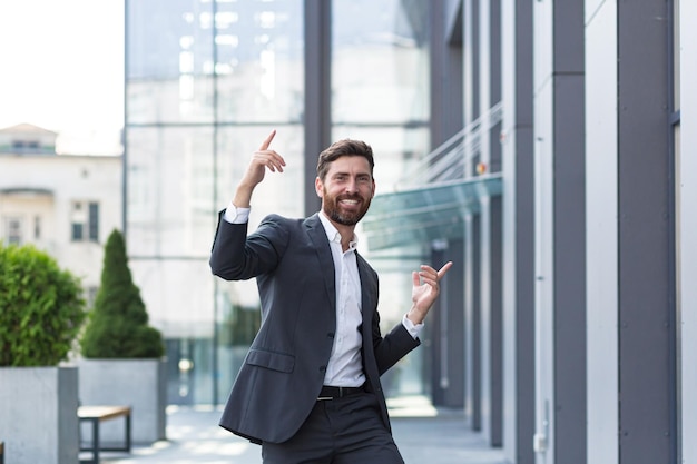 Photo cheerful happy business man dancing walk the city street background a modern office building outside, outdoors funny successful businessman in suit celebtes victory