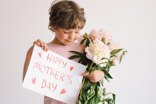 Cheerful happy child with Peonys bouquet Smiling little boy on white background Mothers Day concept