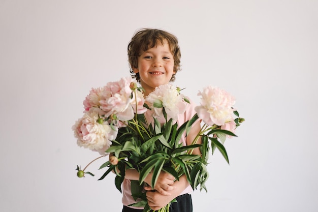 牡丹の花束と陽気な幸せな子供白い背景の上の小さな男の子の笑顔