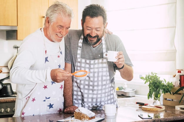 cheerful and happy couple father son middle age and senior mature cooking cake together at home at the kitchen