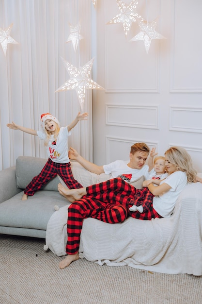 Cheerful and happy family in identical pajamas lying on the sofa Children are having fun Loving family with gifts in the room