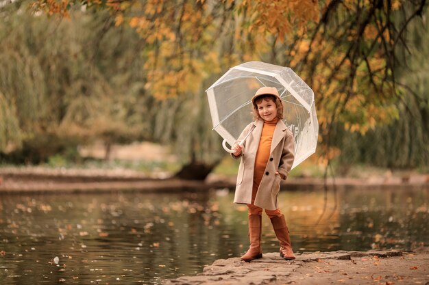 Cheerful happy girl with a transparent umbrella on a walk in the autumn by the lake