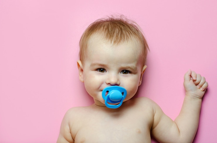 ピンクの背景に横になっている青いおしゃぶりを持つ陽気で幸せな子供男の子。